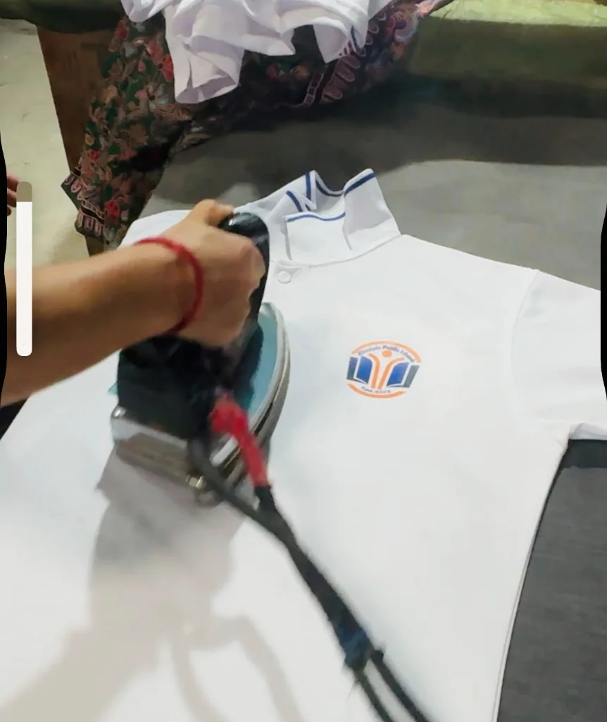 Industrial steam iron pressing a school uniform polo at Pragati Venus Uniform